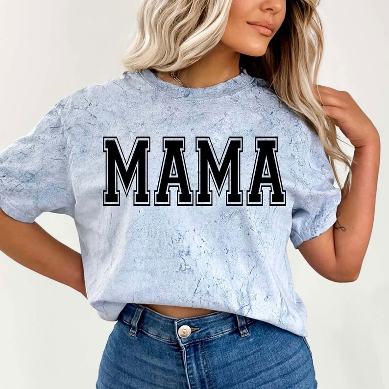 May include: A light blue t-shirt with a white marbled pattern. The shirt has a black block letter design that says "MAMA".