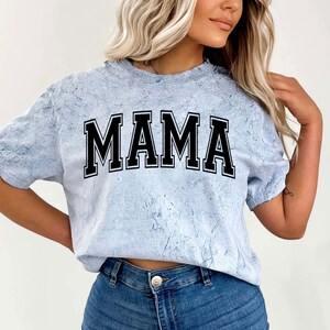 May include: A light blue tie-dye t-shirt with the word "MAMA" printed in black block letters.