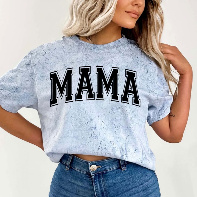 May include: A light blue tie-dye t-shirt with the word "MAMA" printed in black block letters.