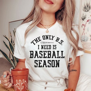 May include: White t-shirt with a black graphic that reads "The only B.S. I need is baseball season". A baseball bat is depicted above the text.