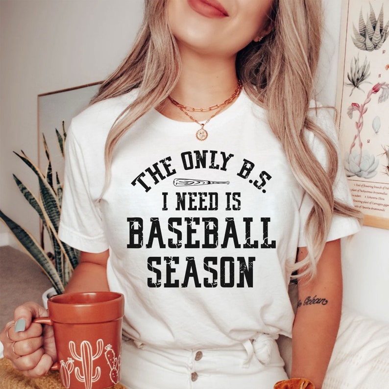 May include: White t-shirt with a black graphic that reads "The only B.S. I need is baseball season". A baseball bat is depicted above the text.