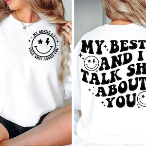 May include: White sweatshirt with black text that reads "My bestie and I talk shit about you" with a smiley face graphic. The text is in a retro font style.