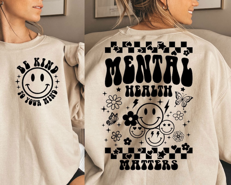 May include: A beige sweatshirt with a black smiley face and the text "Be Kind To Your Mind" on the front and the text "Mental Health Matters" with a black smiley face and other black graphic elements on the back.