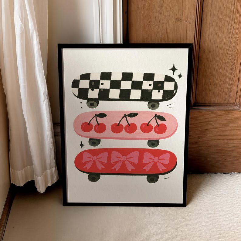 May include: A framed art print featuring three colorful skateboards. The top skateboard has a black and white checkerboard pattern. The middle skateboard is pink with cherries. The bottom skateboard is red with pink bows.
