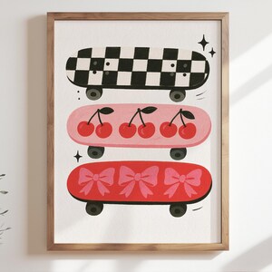 May include: A framed print featuring three colorful skateboards. The top skateboard has a black and white checkered pattern. The middle skateboard is pink with red cherries. The bottom skateboard is red with pink bows. The skateboards have black wheels.