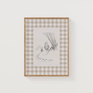 Puede incluir: Una impresión enmarcada con una ilustración en blanco y negro de un oso y un animal más pequeño caminando por un camino. El marco tiene un patrón de cuadros vichy marrón claro.