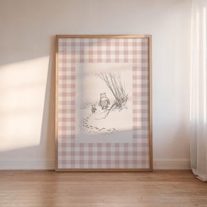 Puede incluir: Obra de arte enmarcada con un boceto a lápiz de un oso y un animal más pequeño caminando en una escena nevada. La obra de arte está sobre un patrón de cuadros rosa y blanco y enmarcada en madera clara.