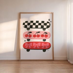 May include: A framed print featuring three skateboards. The top skateboard has a black and white checkerboard pattern. The middle skateboard is pink with cherries. The bottom skateboard is red with bows. All skateboards have black wheels.