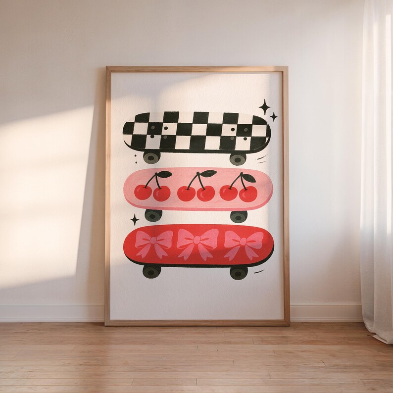 May include: A framed print featuring three skateboards. The top skateboard has a black and white checkerboard pattern. The middle skateboard is pink with cherries. The bottom skateboard is red with bows. All skateboards have black wheels.