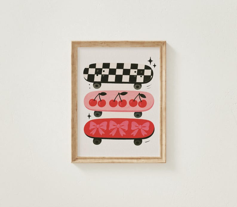 May include: A framed print featuring three skateboards stacked vertically. The top skateboard has a black and white checkerboard pattern. The middle skateboard is pink with cherries. The bottom skateboard is red with bows.