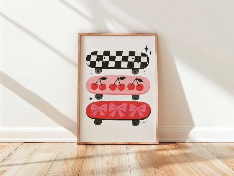 May include: A framed print featuring three skateboards with unique designs. The top skateboard has a black and white checkered pattern. The middle skateboard is pink with cherries. The bottom skateboard is red with pink bows. The print is displayed on a wooden floor.