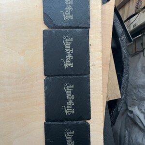 May include: Four black slate coasters with the words "Linds-B-Hall" engraved in a silver colour.