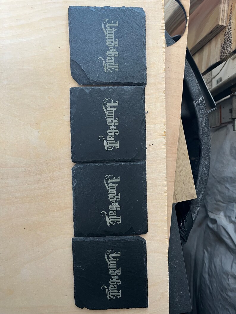 May include: Four black slate coasters with the words "Linds-B-Hall" engraved in a silver colour.