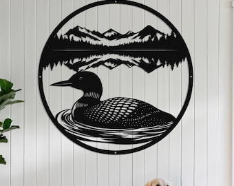 Op de afbeelding: Zwarte metalen wandkunst met een ijsvogel die op het water zwemt, met een berg- en boslandschap op de achtergrond. Het kunstwerk is cirkelvormig en aan een witte muur bevestigd. Een hond zit voor een houten bank.