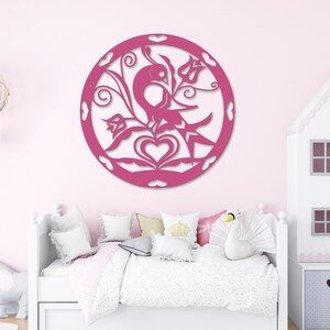 Pode incluir: Decora&ccedil;&atilde;o de parede de madeira rosa com um design circular que apresenta um p&aacute;ssaro, flores e cora&ccedil;&otilde;es. A decora&ccedil;&atilde;o est&aacute; montada em uma parede rosa em um quarto com uma cama branca e uma casa de bonecas branca.