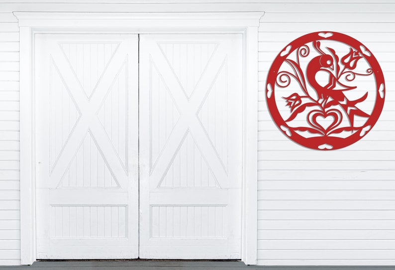 Pode incluir: Arte de parede de metal vermelho com um p&aacute;ssaro estilizado empoleirado em um galho com um cora&ccedil;&atilde;o e flores. A arte &eacute; circular e tem um estilo r&uacute;stico e artesanal.