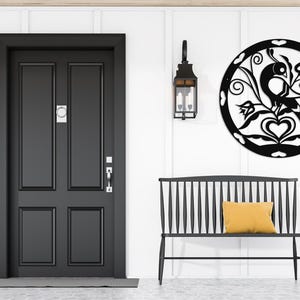 Pode incluir: Decora&ccedil;&atilde;o de parede de metal preto com um p&aacute;ssaro estilizado com flores e cora&ccedil;&otilde;es. A decora&ccedil;&atilde;o est&aacute; pendurada em uma parede branca acima de um banco preto.