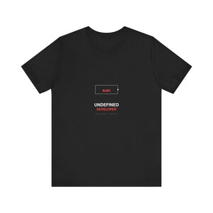 Pode incluir: T-shirt preta com o texto "No%" dentro de um ícone de bateria e as palavras "UNDEFINED DEVELOPER" em vermelho. Abaixo, uma linha de texto menor. A t-shirt tem gola redonda e mangas curtas.
