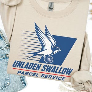 May include: A beige crewneck sweatshirt featuring a graphic of a white swallow bird in flight carrying a bowling ball. The design includes a blue trapezoid shape, motion lines, and the text UNLADEN SWALLOW PARCEL SERVICE in blue and red.