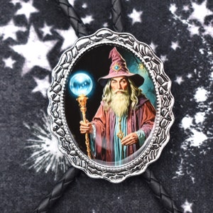 May include: A silver bolo tie with a round, ornate frame featuring a wizard holding a staff with a glowing orb. The wizard is wearing a purple and blue robe and a pointed hat with a blue gem.