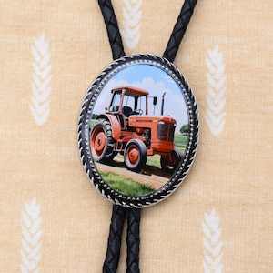 May include: A red tractor with a black and silver bolo tie. The bolo tie has a round pendant with a picture of the tractor on it.