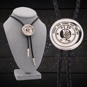 May include: A silver bolo tie with a black braided leather cord. The circular pendant features a weather gauge design with the words "Stormy Rain Change Fair Very Dry" around the edge. The tie is displayed on a gray mannequin.