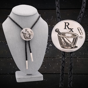 May include: A black bolo tie with a silver pendant featuring a mortar and pestle with the symbol "Rx" and pills.
