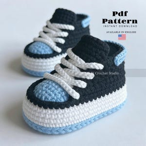 Puede incluir: Un par de zapatillas de bebé hechas a mano con ganchillo en negro, blanco y azul claro. Las zapatillas tienen cordones blancos y puntera y talón azul claro. La imagen incluye el texto "Pdf Pattern" y "Instant Download".