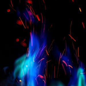 Puede incluir: Imagen abstracta de llamas azules y rojas con chispas volando en el aire. Las llamas están sobre un fondo negro.