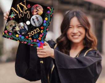 May include: A black graduation cap decorated with colorful flowers and the text "My Why 2023". The cap has a tassel and is held by a person wearing a black graduation gown.