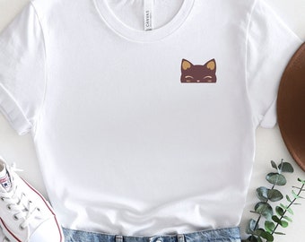 May include: White t-shirt with a small brown cat face graphic on the front. The shirt is paired with light blue denim shorts and white sneakers.