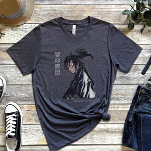 May include: A dark heather grey t-shirt with a black and white illustration of a samurai warrior. The shirt has the Japanese text "日本武道" printed on the right side of the image. The text translates to "Japanese Martial Arts".