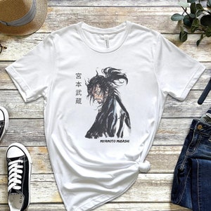 May include: White t-shirt with a black and white illustration of a samurai warrior with the text "Miyamoto Musashi" and Japanese characters that read "宮本 武蔵".