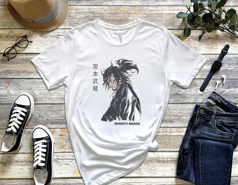 May include: White t-shirt with a black and white illustration of a samurai warrior with the text "Miyamoto Musashi" and Japanese characters that read "宮本 武蔵".
