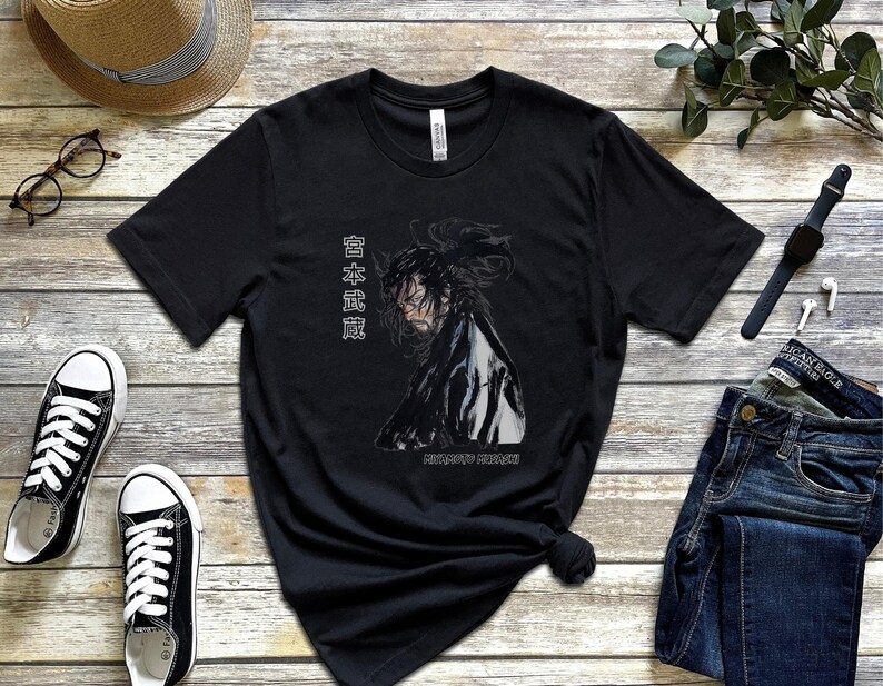 May include: Black t-shirt with a graphic of a person with long black hair and a white shirt. The text "日本武道" is printed on the shirt.