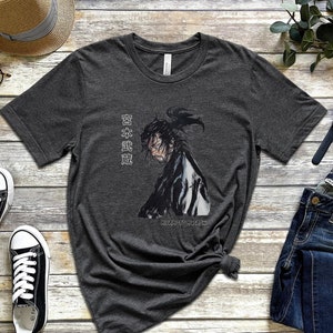 May include: A dark heather grey t-shirt with a black and white illustration of a samurai warrior. The Japanese text on the shirt reads "日本武道".