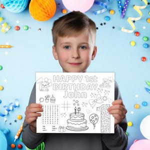 Puede incluir: Un ni&ntilde;o sostiene una p&aacute;gina para colorear blanca con el texto "HAPPY 1st BIRTHDAY John" en negro. La p&aacute;gina presenta ilustraciones de una tarta, globos y un laberinto. El fondo est&aacute; decorado con globos de colores, confeti y serpentinas.