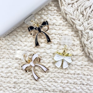 May include: Three gold-tone bow charms with enamel accents. One bow is black, one is white, and one is white with a gold center.