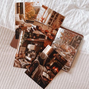 May include: A collection of rectangular photographic prints featuring warm autumn-themed scenes, including a cozy window nook, a rustic kitchen with pumpkins, a cream-colored espresso machine, a fireplace with a book, and a decorated dining table.