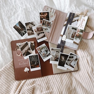 May include: A brown leather planner with polaroid photographs, a pearl necklace, and a decorative flower pin. The planner is open, with a pink leather case and a ribbon visible. The photos depict various scenes.