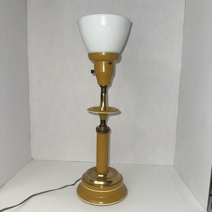 May include: A vintage table lamp with a white, textured, cone-shaped shade. The lamp has a mustard yellow base and stem with brass accents. The base is round with a white trim. A black cord extends from the base.