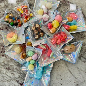 May include: Assortment of colorful candies and treats packaged in small, iridescent, resealable bags. The bags are filled with various shapes and colors of candy, including gummies, marshmallows, and chocolate.