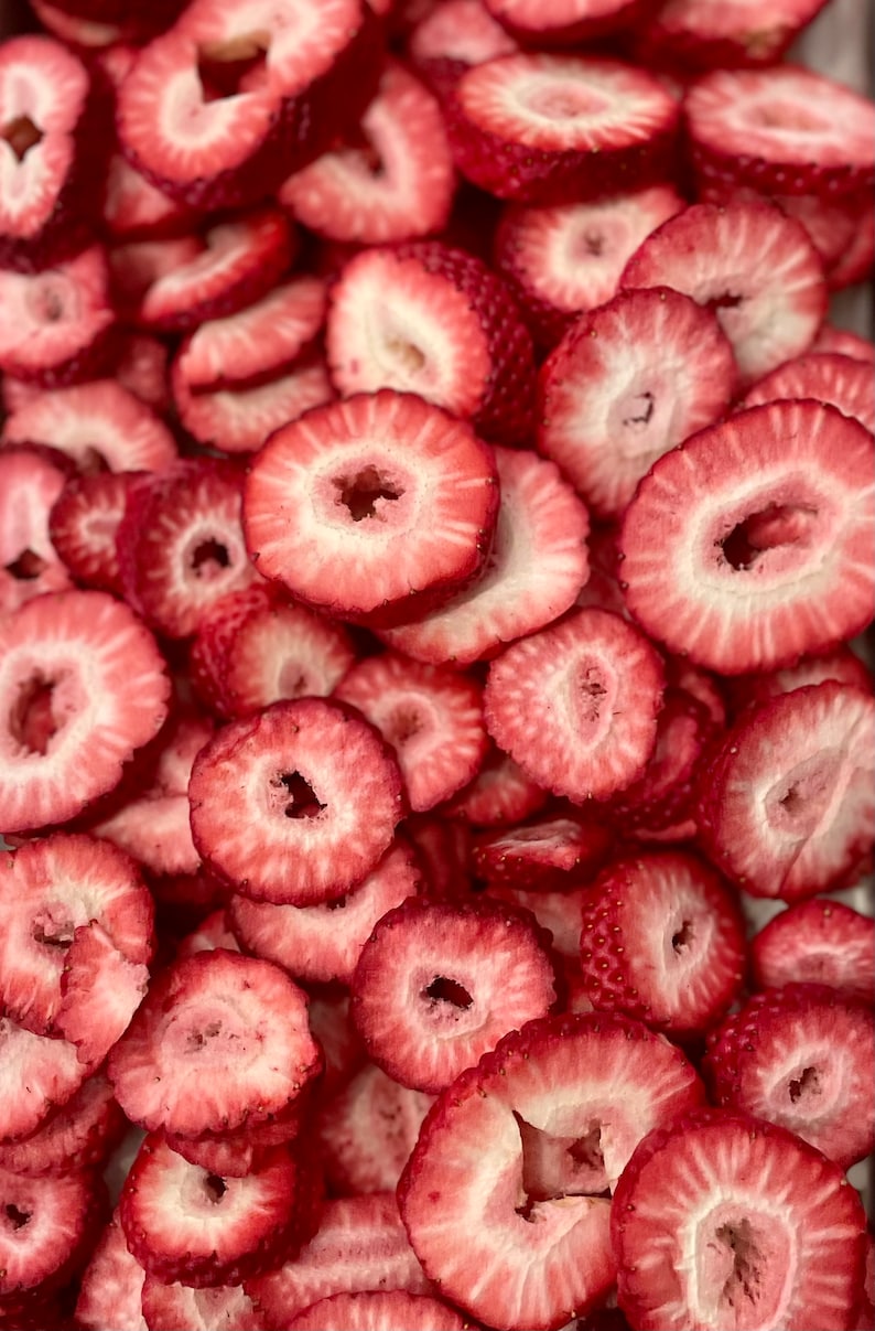 May include: A close-up image of a pile of dried strawberry slices. The slices are a vibrant red color and have a slightly translucent appearance.