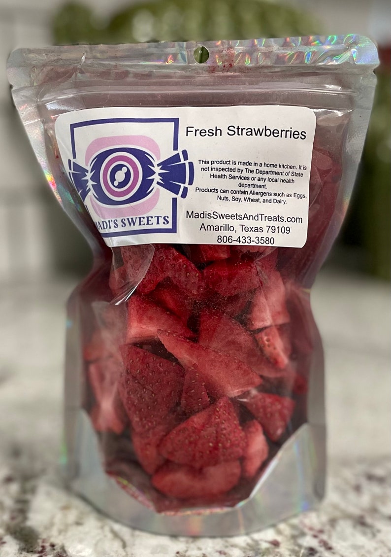 May include: A clear plastic bag filled with fresh, red strawberry slices. The bag has a label that reads "ADI'S SWEETS" and "Fresh Strawberries". The label also includes information about the product being made in a home kitchen and not inspected by the Department of State Health Services. It also includes the website and phone number for Madis Sweets And Treats.