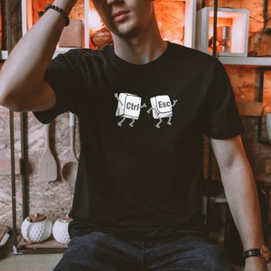 May include: A black t-shirt with a white graphic of two computer keys, "Ctrl" and "Esc", with legs and arms, dancing.