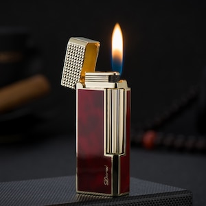 May include: A gold and red lighter with a flame coming out of the top. The lighter has a textured lid and the word "Derui" is printed on the side.