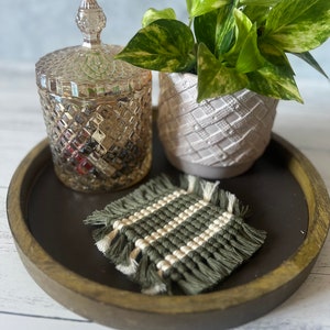 May include: A wooden tray with a green and white woven coaster, a clear glass jar with a lid, and a potted plant with green and yellow leaves.