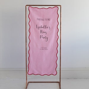 K&ouml;nnte beinhalten: Rosa Stoffbanner mit gewellten R&auml;ndern und einem Kupferst&auml;nder. Das Banner lautet "From Miss to Mrs Isabella's Hens Party 22.07.2023 35 Days to Go".