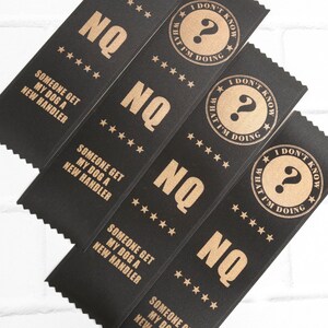 May include: Four black satin ribbons with gold text. The ribbons say "NQ" and "Someone get my dog a new handler."  The ribbons also have a gold circle with a question mark and the text "I don't know what I'm doing."