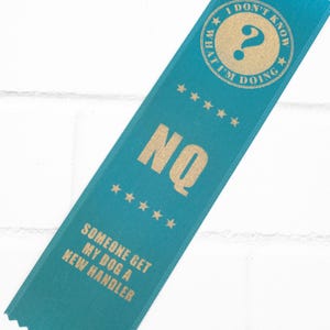 May include: A blue ribbon with gold text that reads "I don't know what I'm doing" and "NQ" with five gold stars. The ribbon also says "Someone get my dog a new handler".